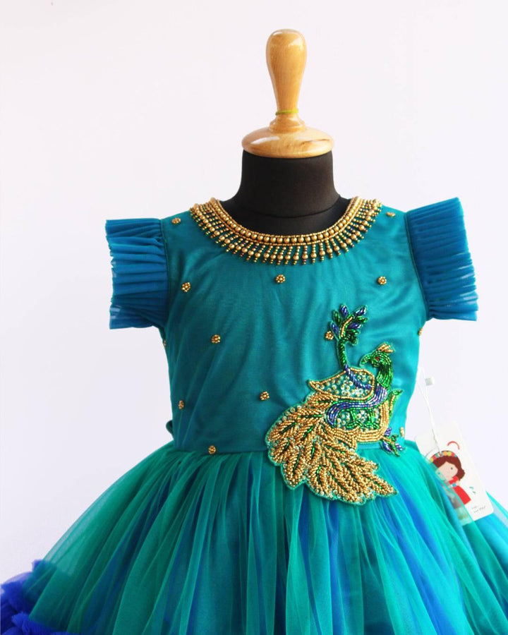 Peacock theme Applique Party wear Frock.
Material: Royal blue and Tourqise green colour net is using in the main portion of the dress. Royal blue colour net is pleating in the bottom portion. Over all colo