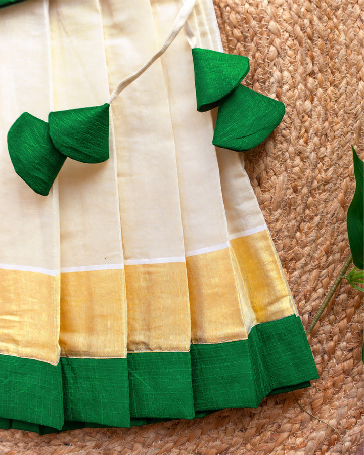 Close-up of the traditional Kasavu border on a cream green Onam lehenga choli for baby girl.